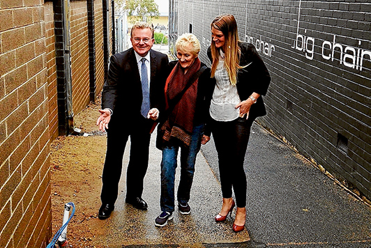 Hasten slowly: Federal MP Bruce Billson, Judy Edwards and Kim Rowe of Mornington Chamber of Commerce inspect CCTV and lighting wiring in one of the laneways between Main St and McLaren Place. Poles were installed last week. Picture supplied