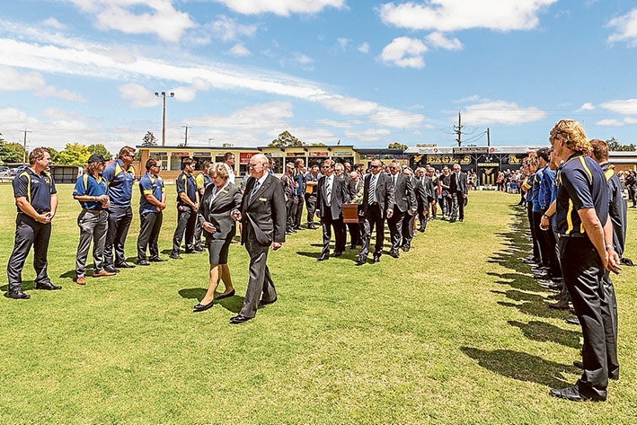 Ground of honour: Leanne Gomm and funeral director Ted Bull lead the funeral procession for her husband Murray Gomm through a guard of honour at Somerville Football Oval on Monday. Picture: Gary Sissons