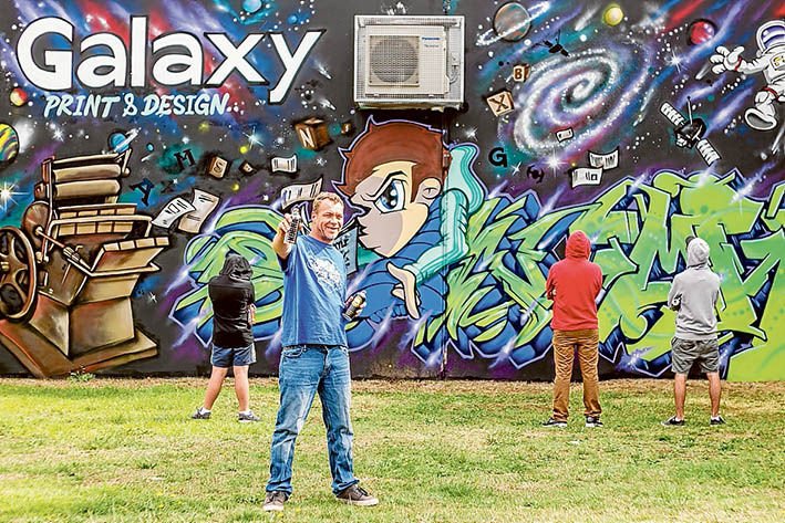 Art mix: Michael “Mikey” Newman, above, has mixed graffiti and art on the factory wall of a printer at Hastings in a bid to involve taggers and avoid a repetition of the previous unsightly “art” that covered the wall, below. Pictures: Yanni