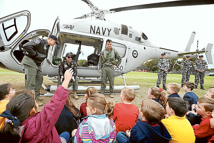 Looking good: St Joseph’s pupil Madison Cruickshank, below, tries on a helicopter pilot’s helmet during the Navy 723 Squadron visit to Cyril Fox Reserve, Crib Point. Above, Sub Lieutenant Frank Tachibana (right), Lieutenant Tristram Gleeson (centre) and Sub Lieutenant Olie Bohling fielding questions from Crib Point Primary pupils.